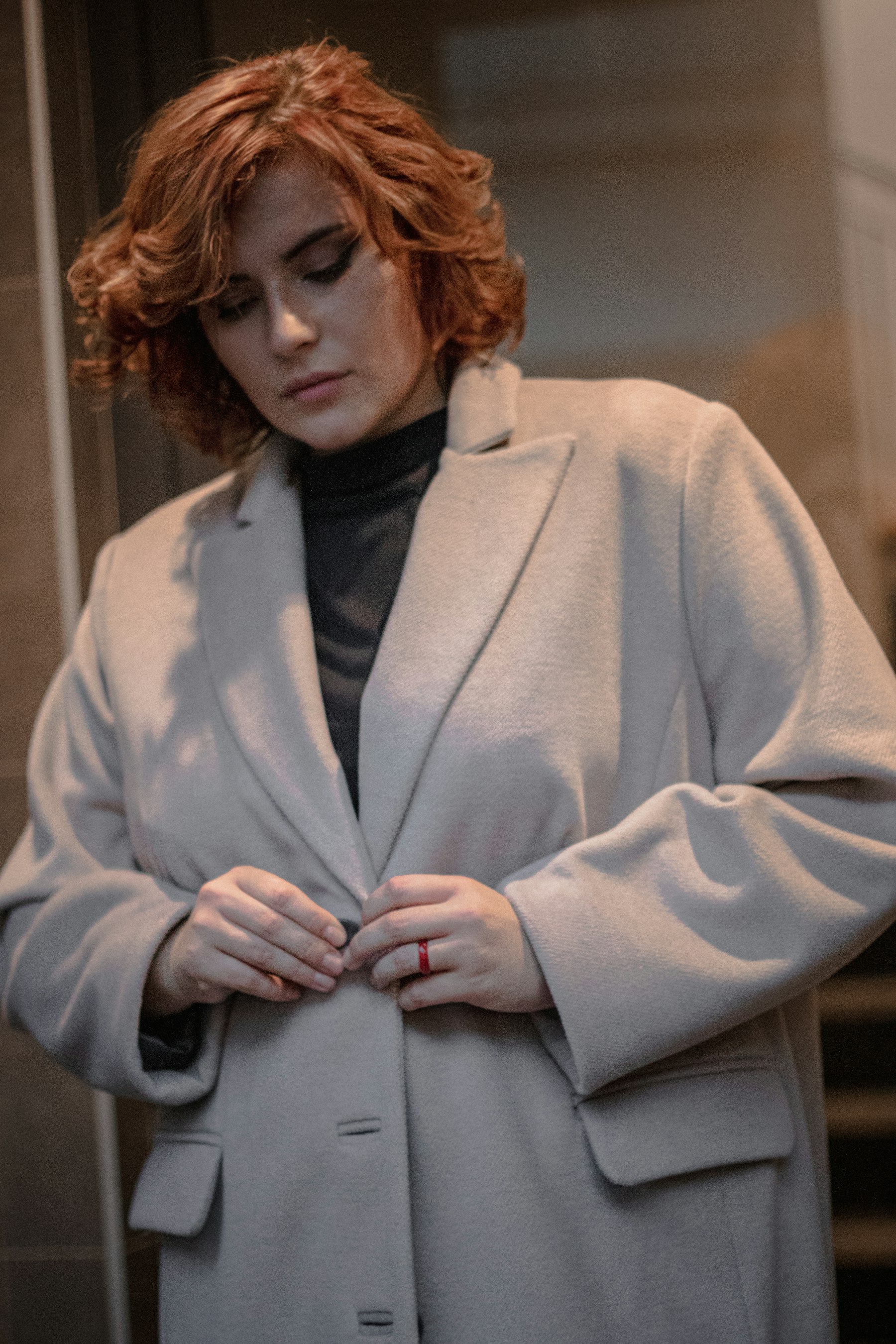 Mujer con abrigo de lana gris claro abrochándose un botón, en una luz suave — imagen ilustrativa